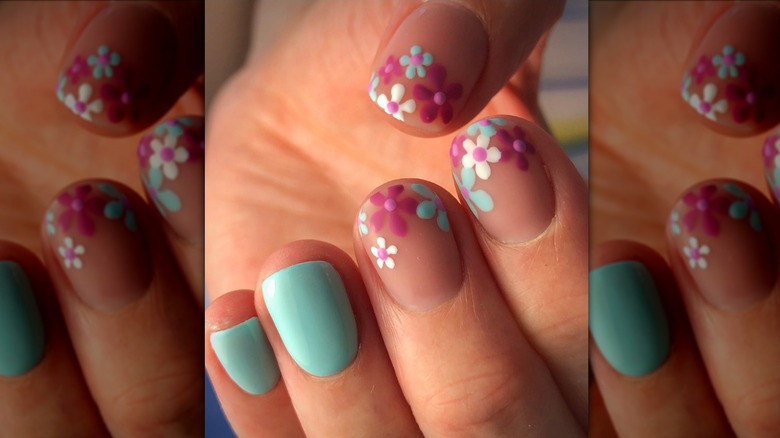 Imagen de cerca de una manicura con dos uñas de color azul claro y tres uñas con flores rosas y azules.