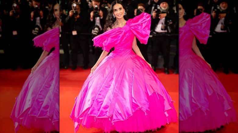 Demi Moore posando para una foto con un vestido rosa intenso de aspecto hortera con un gran lazo de Matières Fécales en el Festival de Cine de Cannes de 2026
