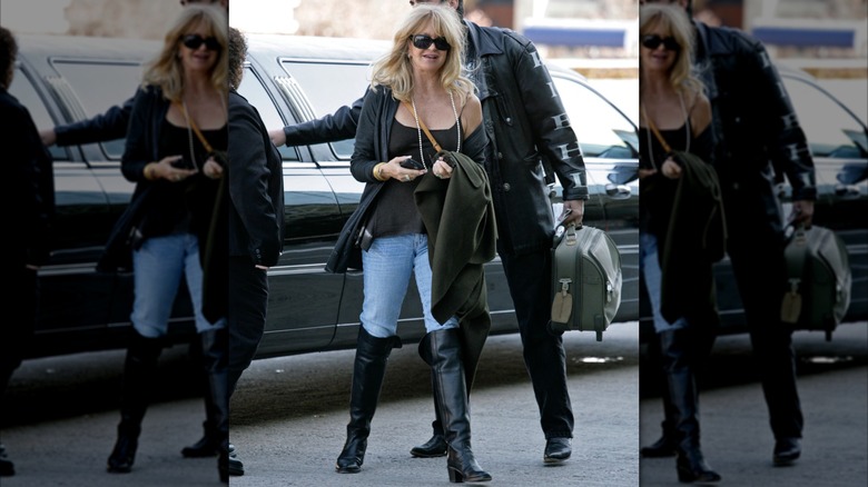 Goldie Hawn fotografiada cerca de un automóvil en una calle con jeans, botas negras, una blusa negra y gafas de sol.