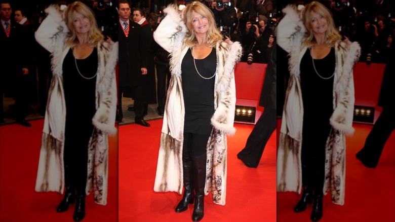 Goldie Hawn en un evento de alfombra roja con un traje completamente negro y un abrigo largo y sedoso con ribete de piel.