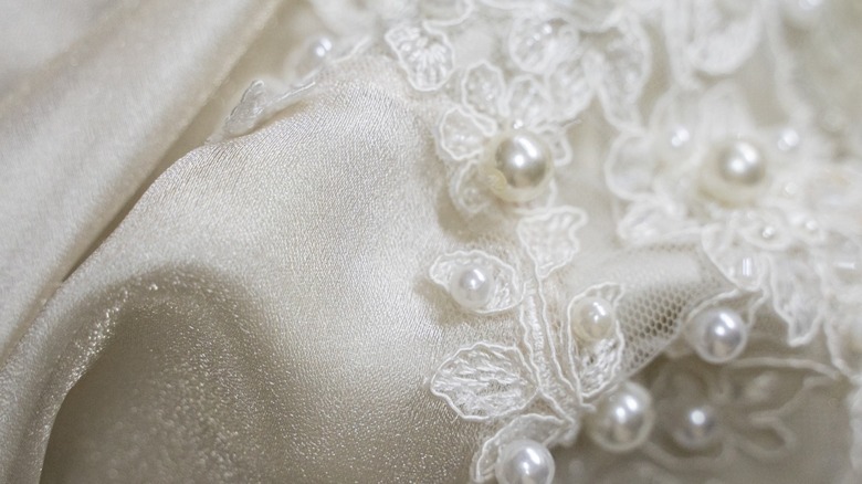 Una imagen de primer plano de un vestido de novia con encaje y perlas.