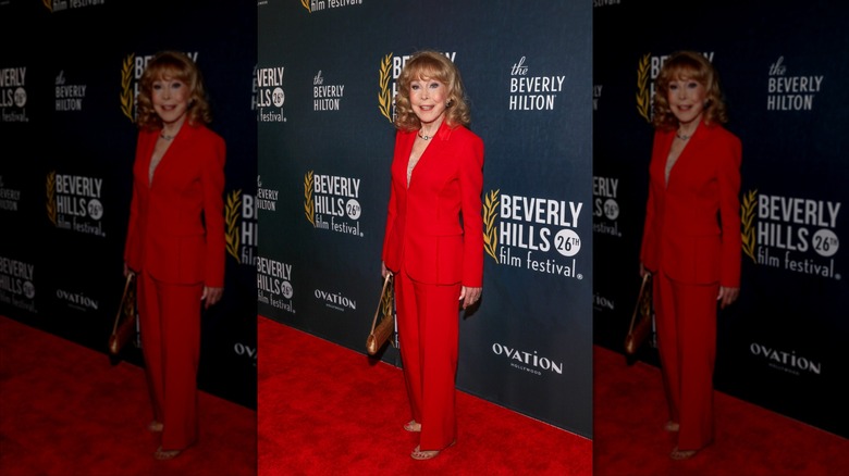 Barbara Eden sonríe luciendo un traje pantalón rojo