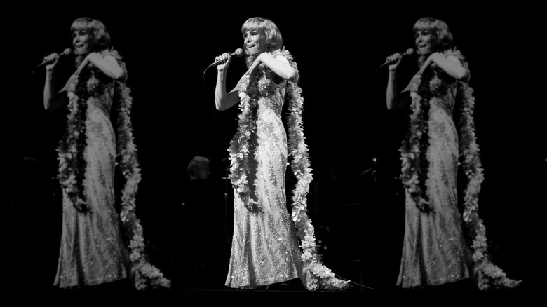 Barbara Eden sostiene un micrófono con un vestido adornado en oro y una boa de plumas.