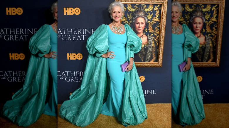 Helen Mirren posando frente a un cuadro en 2019 con un vestido color aguamarina con una capa abullonada y joyas llamativas.