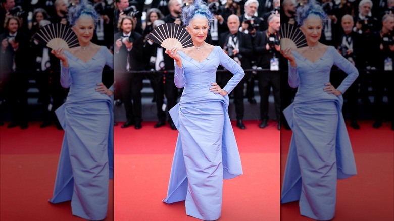 Helen Mirren sosteniendo un abanico en la alfombra roja en 2023 con un vestido bígaro y cabello a juego.