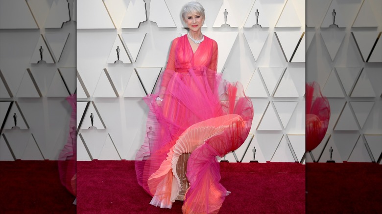 Helen Mirren posando en la alfombra roja en 2019 con un vestido rosa brillante con una falda que ondea al viento.