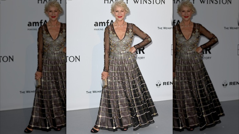 Helen Mirren posando con la mano en la cadera en un evento en 2016 con un detallado vestido negro y plateado.
