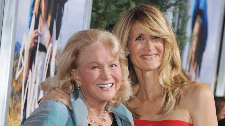 Laura Dern luce un vestido rojo sin tirantes en la alfombra roja mientras se agarra del hombro de su madre Diane Ladd, vestida con una chaqueta azul claro.