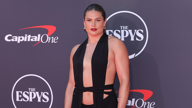 Ilona Maher posando en la alfombra roja con un vestido negro recortado y el pelo recogido en una cola de caballo en The ESPYS.