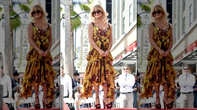 Goldie Hawn luce un vestido con volantes color mostaza y gafas de sol.