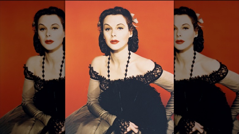 Hedy Lamarr con un vestido beige con encaje negro y sosteniendo un abanico