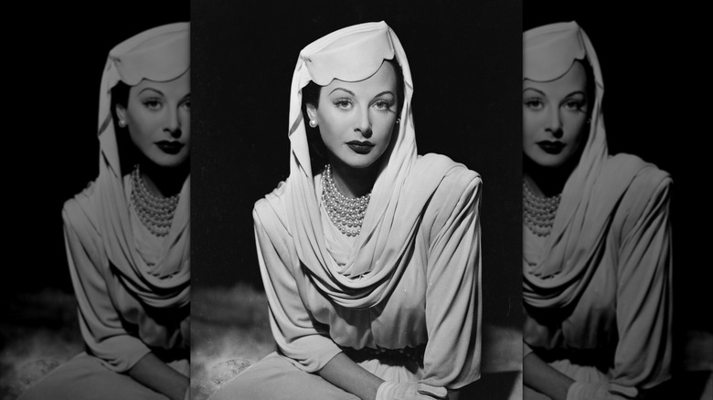 Hedy Lamarr lleva un sombrero tipo pastillero, perlas y un pañuelo en la cabeza.