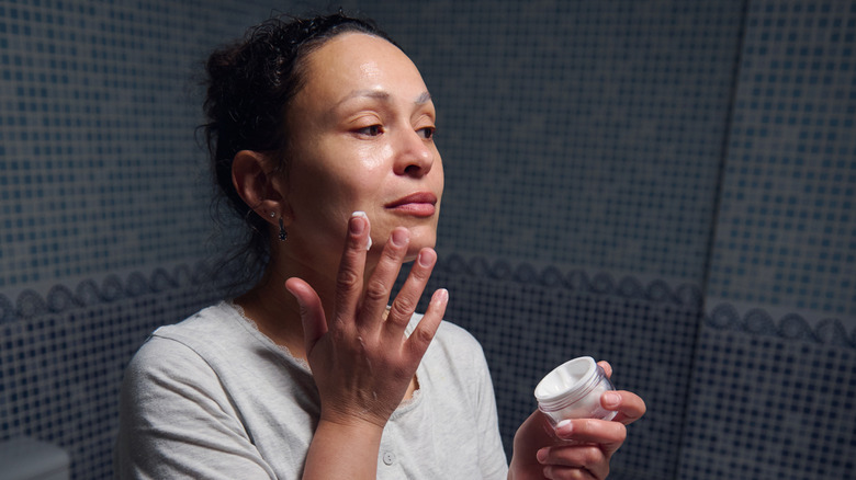 Una mujer mayor aplicándose crema en la piel.