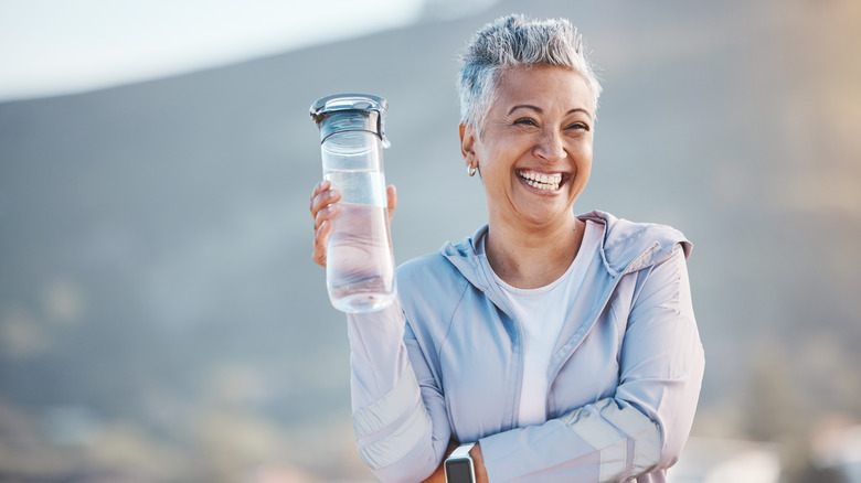 Una mujer mayor bebiendo agua de una botella de vidrio.