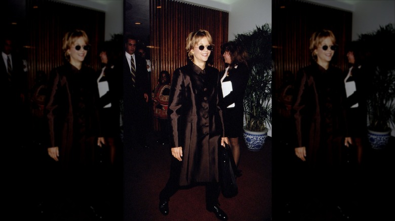 Meg Ryan sonriendo y luciendo un abrigo marrón y gafas de sol.