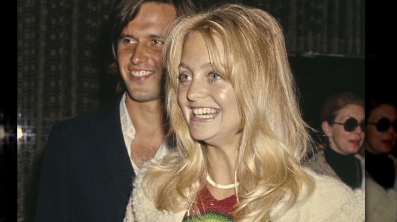 Goldie Hawn sonriendo sin maquillaje con un suéter blanco y un collar blanco.
