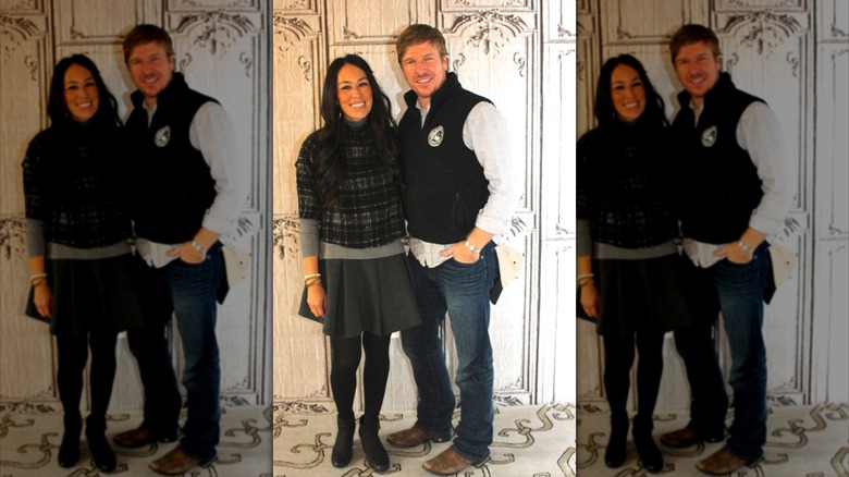 Joanna Gaines y Chip Gaines posando juntos contra una pared blanca ornamentada.