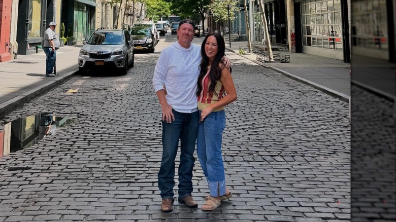 Chip Gaines con jeans y una camiseta y Joanna Gaines con una camiseta sin mangas y jeans posan abrazados.