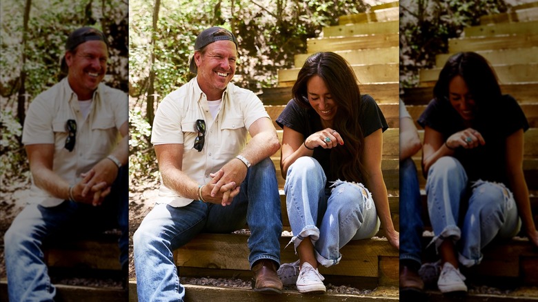 Chip Gaines con una camisa blanca y jeans con una gorra al revés y Joanna Gaines con jeans y una camiseta negra riéndose juntos sentados en las escaleras.