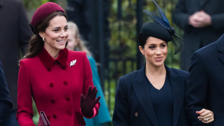 Meghan Markle, vestida de negro, y Kate Middleton, vestida de rojo, fotografiadas juntas llegando a un servicio religioso el día de Navidad.