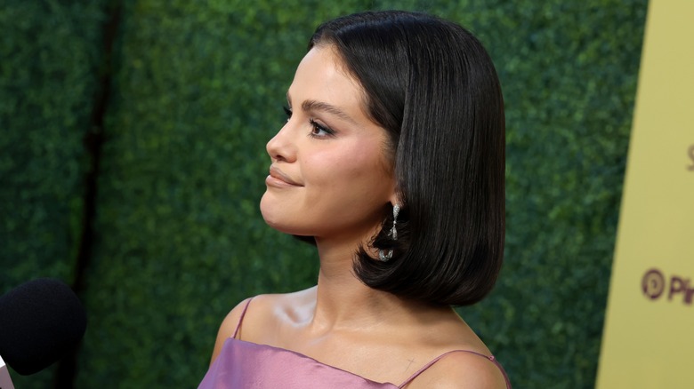 Selena Gomez posa frente a un fondo verde en un evento, con un elegante peinado bob.