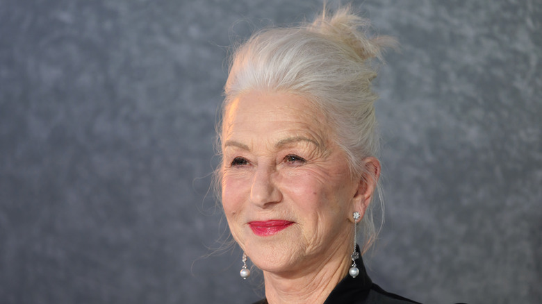 Helen Mirren posando sobre un fondo gris con pendientes y el pelo recogido.