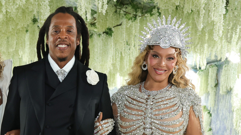 Jay-Z con un traje negro y Beyoncé con un conjunto adornado de cristales posando juntos en un evento.