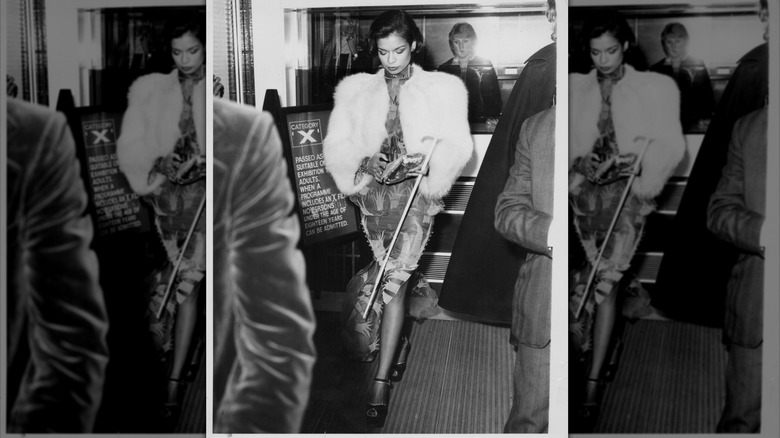 Bianca Jagger mirando hacia abajo con un abrigo de piel blanco y sosteniendo un bastón.