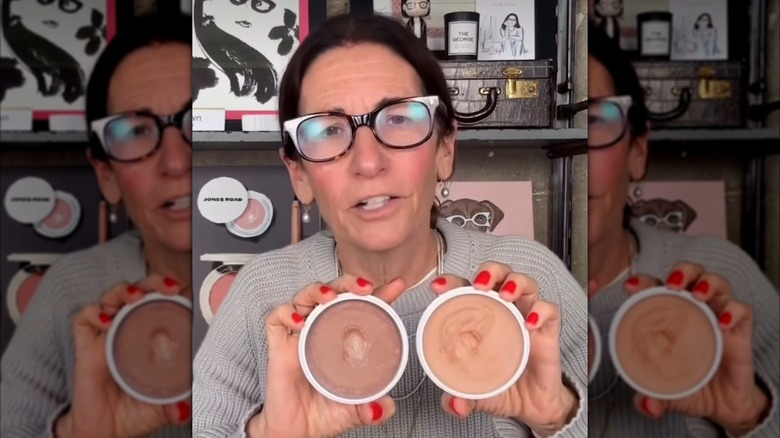 Bobbi Brown con gafas sosteniendo uno de los productos de su marca, Miracle Balm.