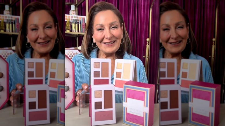 Laura Geller posando con paletas de maquillaje frente a ella.