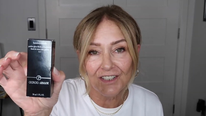 Mujer con una camiseta blanca sosteniendo un contenedor de Giorgio Armani Luminous Silk Foundation.
