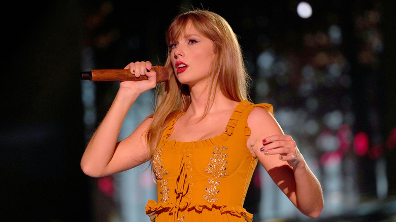 Taylor Swift usa un vestido naranja mientras canta en el escenario y mira con nostalgia al público.