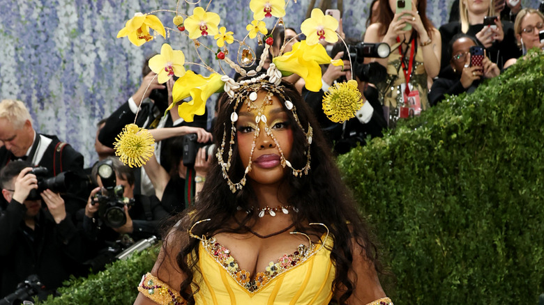 Sza posando en la Met Gala con un tocado floral y un corpiño amarillo.