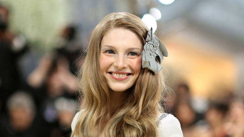 Hunter Schafer sonriendo en la Met Gala 2026 con un lazo gris en el pelo.