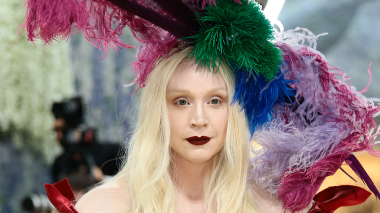 Gwendoline Christie posando en la Met Gala 2026 con el pelo suelto luciendo un gran sombrero de plumas y lápiz labial rojo oscuro.