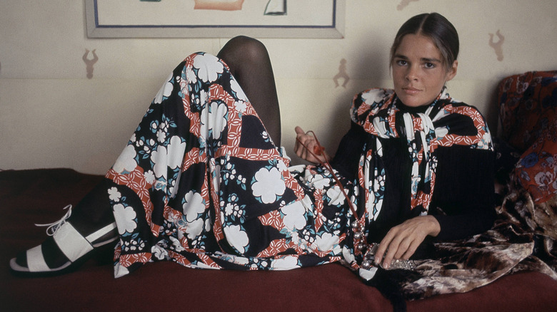 La actriz Ali MacGraw descansando en un sofá luciendo un conjunto de inspiración asiática con zapatos blancos.