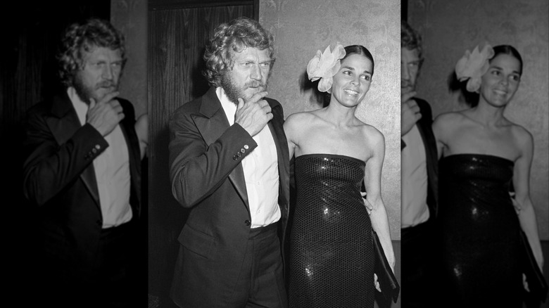 Ali MacGraw luciendo un vestido negro palabra de honor y adorno floral en el cabello sonriendo junto a Steve McQueen luciendo un traje.
