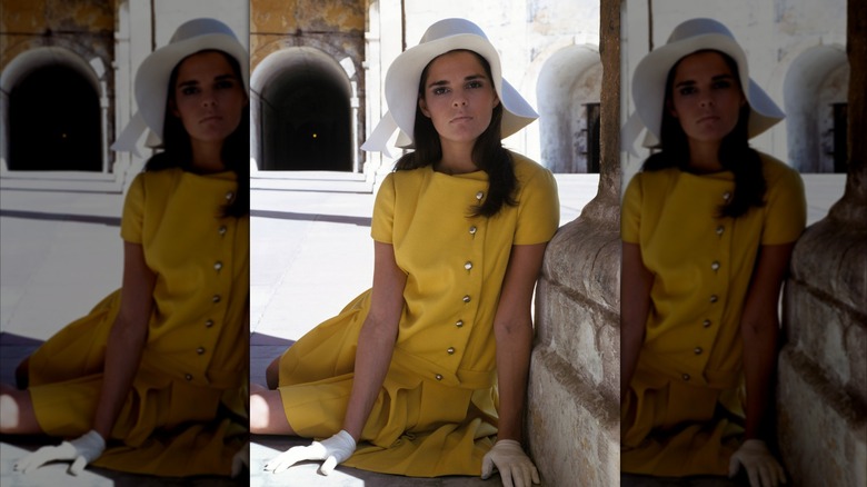 Ali MacGraw vistiendo un traje de lana amarillo con guantes blancos y un sombrero blanco.