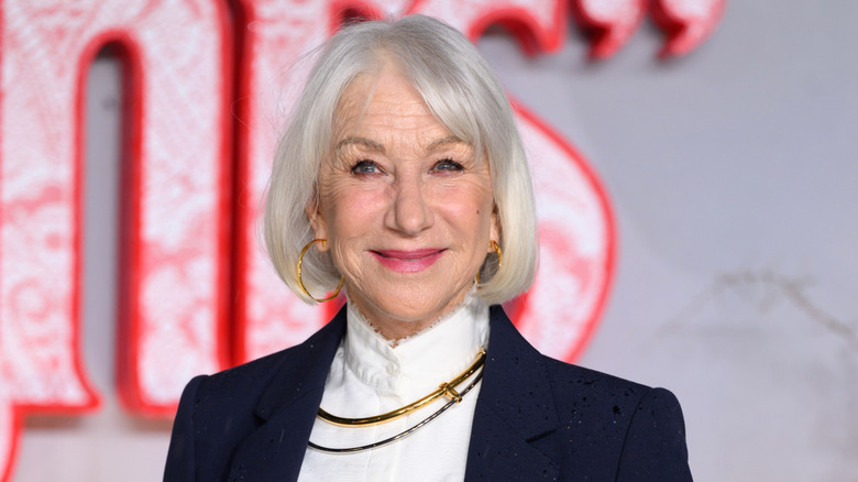 La actriz Helen Mirren sonriendo y luciendo aros y una chaqueta.