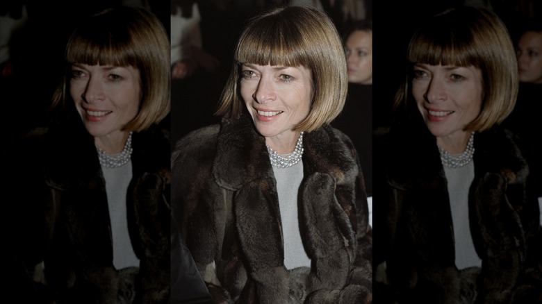 Anna Wintour sonríe con cabello rubio miel y luce una chaqueta de piel y un collar de perlas.