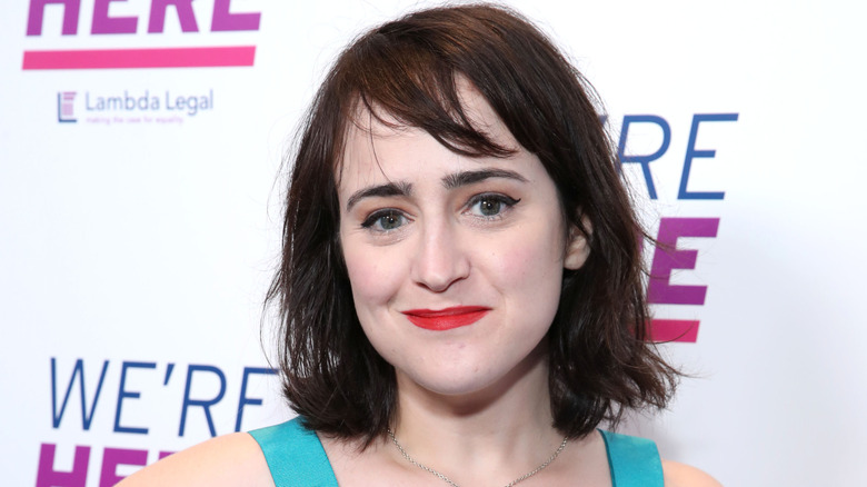 Mara Wilson con un vestido turquesa con labios rojos en una alfombra roja.