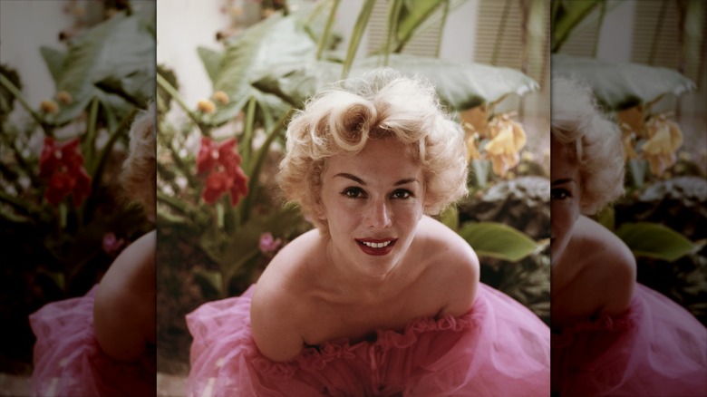 Eva Gabor sonríe luciendo labial rojo y un vestido de tul rosa.
