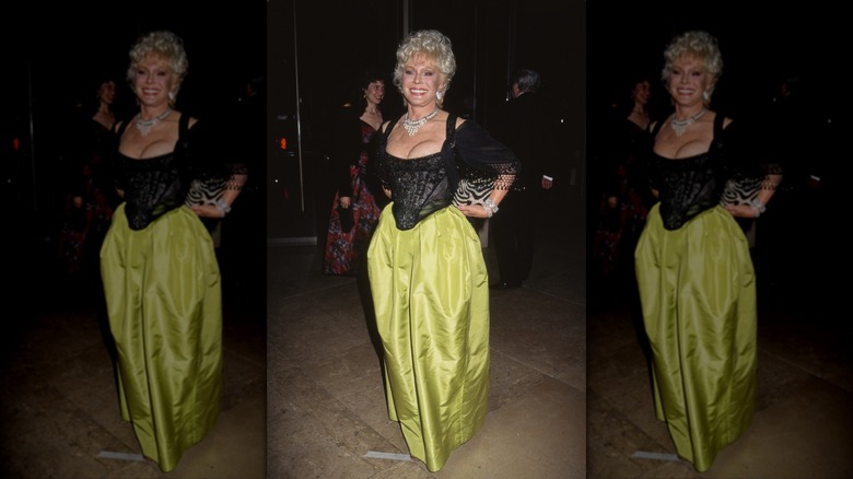 Eva Gabor sonríe con un corsé negro, una falda verde y un collar llamativo.