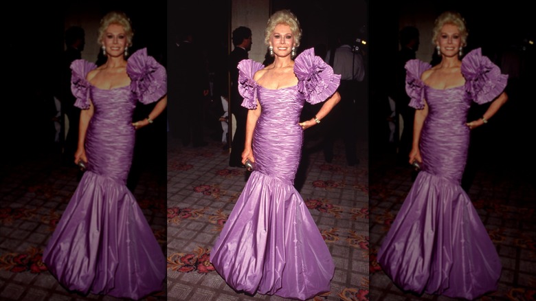 Eva Gabor sonríe con un voluminoso vestido lila con mangas abullonadas.