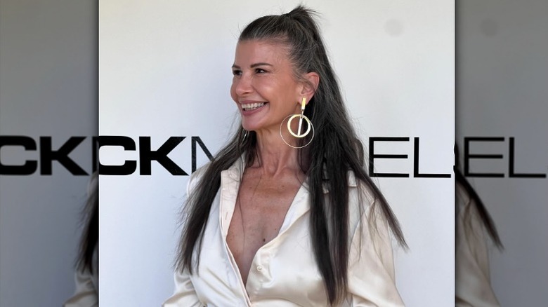 Una mujer sonriendo en un evento con el cabello medio recogido y una blusa sedosa y aretes llamativos.