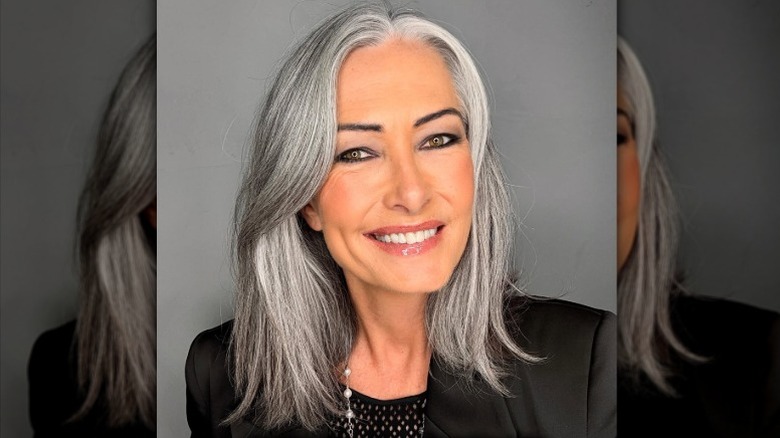 Una mujer con cabello gris de longitud media sonriendo y vestida con un top y una chaqueta negros.
