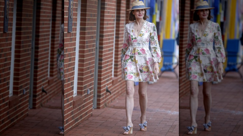 Geena Davis luciendo un vestido blanco con flores y un sombrero de paja mientras camina