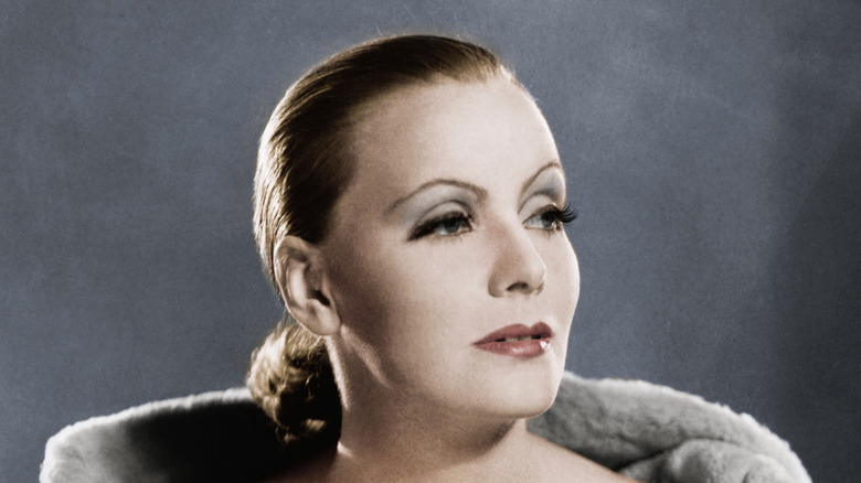 Greta Garbo fotografiada con un moño bajo posando sobre un fondo gris.