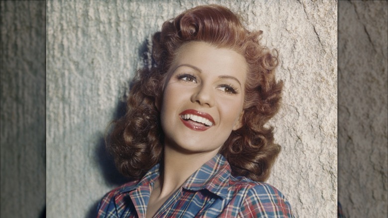 Rita Hayworth sonriendo con una camisa a cuadros y cabello rojo rizado.