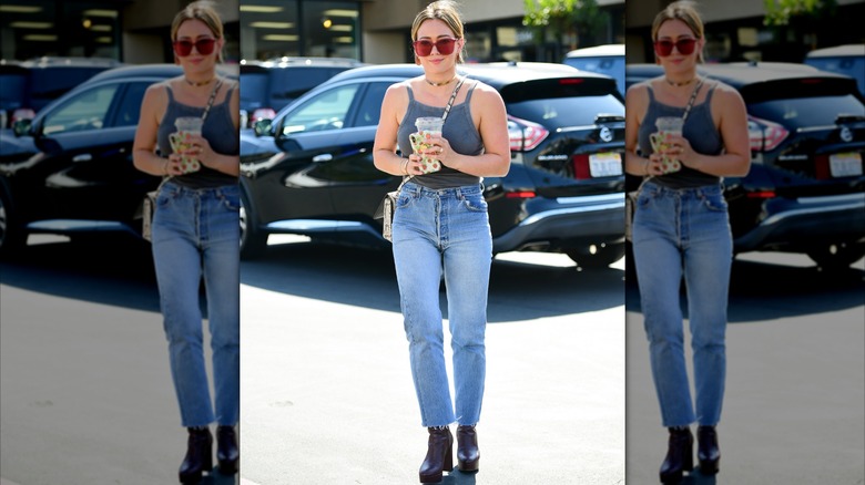 Hilary Duff fue fotografiada en la calle sosteniendo una taza y vistiendo una camiseta sin mangas gris, jeans, botas negras y gafas de sol rojas.